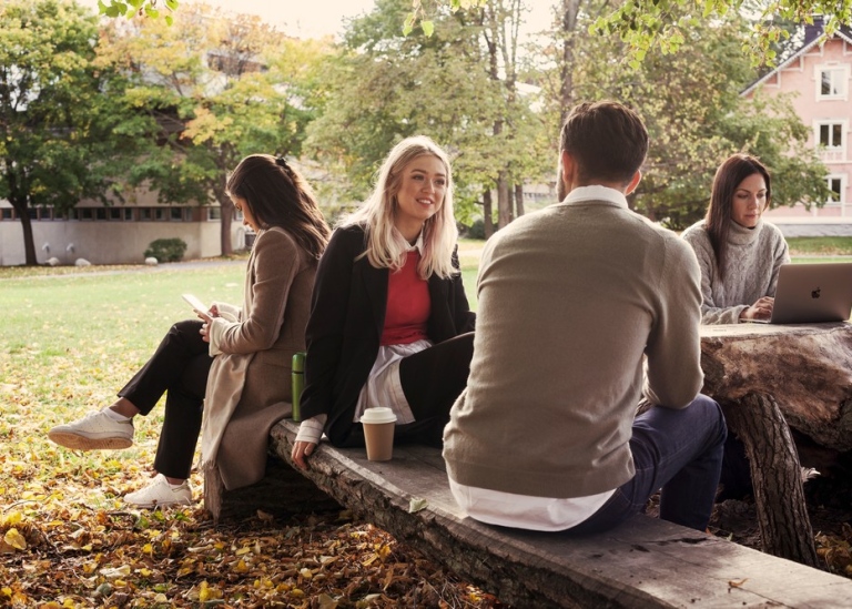 Foto på studenter som sitter på en bänk i campus Frescati då det är hösten.
