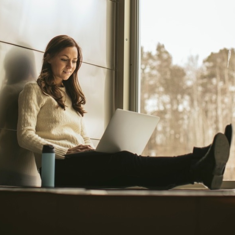 A girl with a laptop sitting in a large window.
