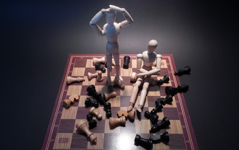 Chessboard with scattered pieces and two wooden dolls. Photo: Succo from Pixabay.
