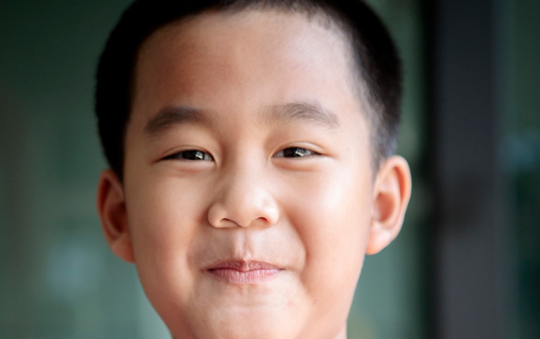 Asiatisk pojke ca 6 år ler lite spjuveraktigt. Foto: khunaspix, MostPhotos