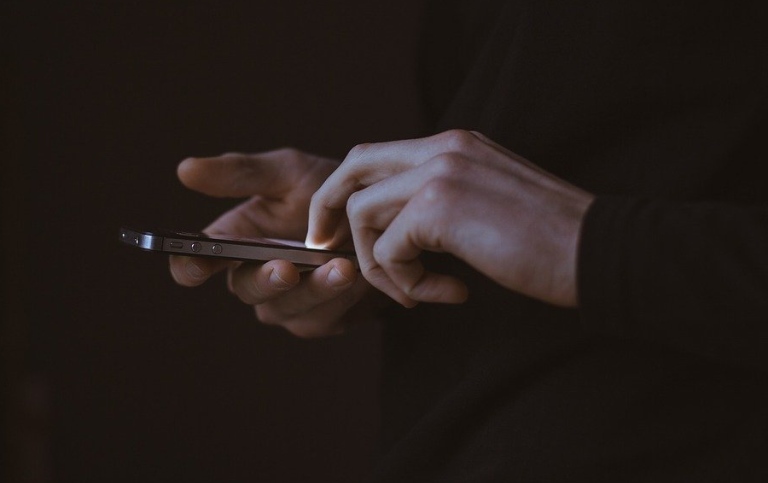 Hands using a mobile screen in the dark. Photo: Free-Photos from Pixabay.