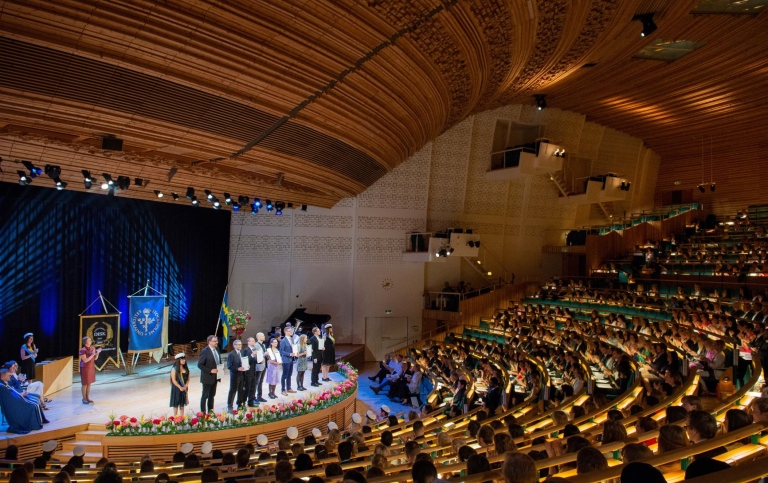 Aulan full av festklädda studenter som tagit examen.