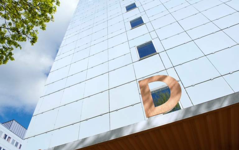 Building D.Light blue glass facade, an orange D, from a worm's-eye view.