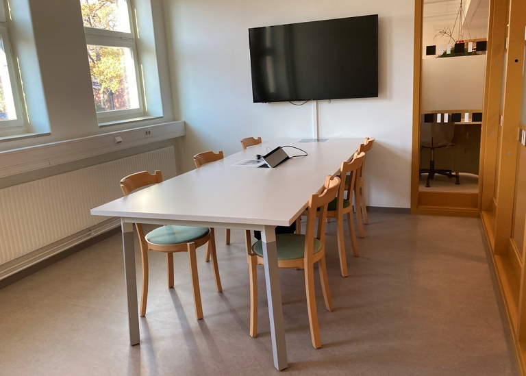 Room with a table and chairs for six persons, tv-screen and whiteboard.