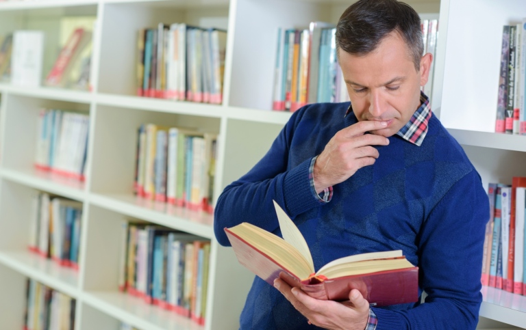 Fundersam man läser i en bok i bibliotek