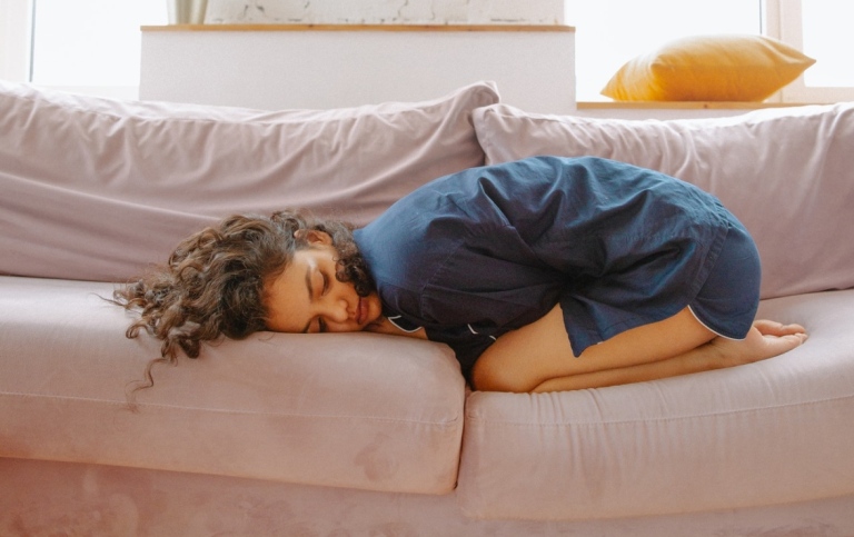 Kvinna med magont ihopkrupen i en soffa.