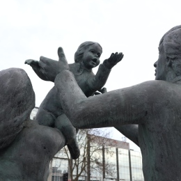 Statyer av vuxna som båda sträcker sig efter ett barn.