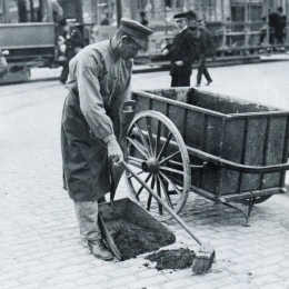 svartvitt foto av man i gammaldags kläder som sopar upp avfall på gatan.