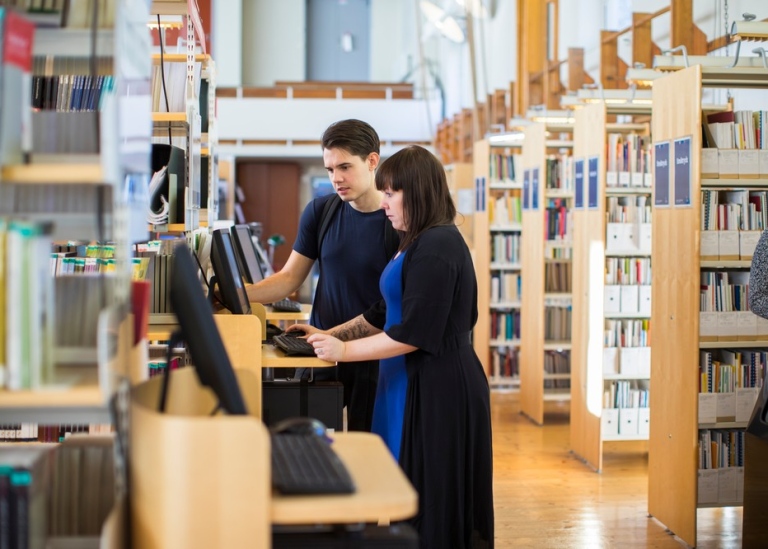 Studenter söker på dator i ett bibliotek