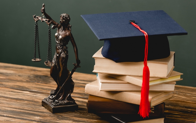 graduation hat on a pile of books and a statue of the lady justice next to it