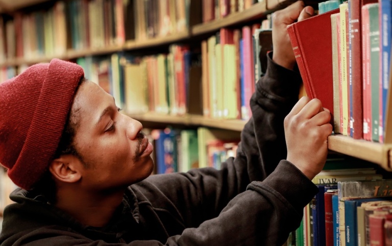 Student tar en bok från en bokhylla.