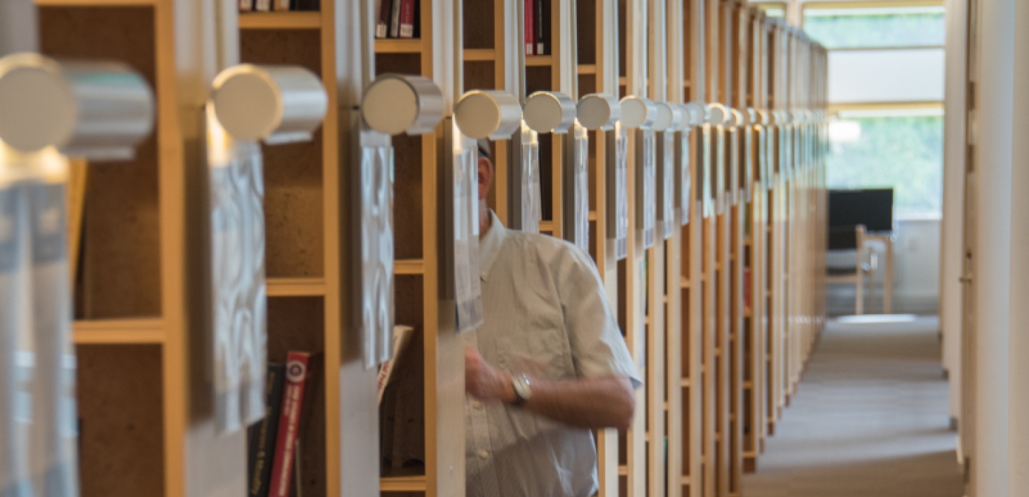 An elderly man looks at books in a row of bookshelves