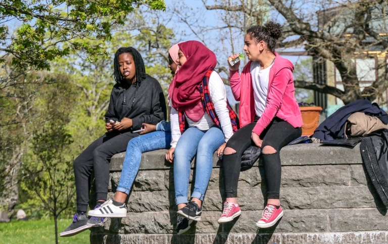 Multietnisk tjejgrupp i tonåren sitter utomhus.