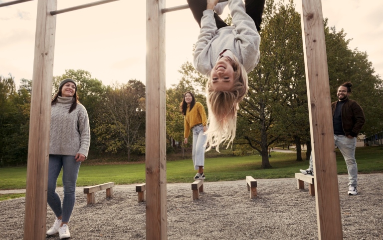 Studenter som hänger i stänger på utomhusgym. Text För att du vill göra skillnad på hög nivå. 