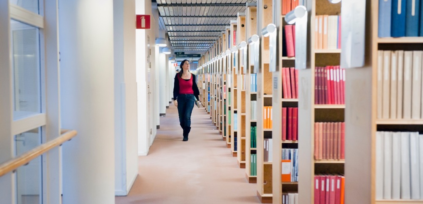 Woman walking alongside book shelves.