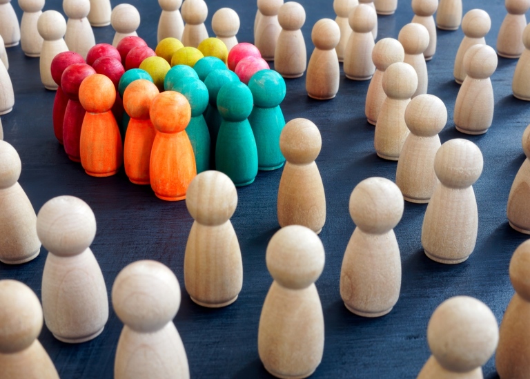 Idébild social inkludering - en grupp spelpjäser i olika färger står i grupp tillsammans.