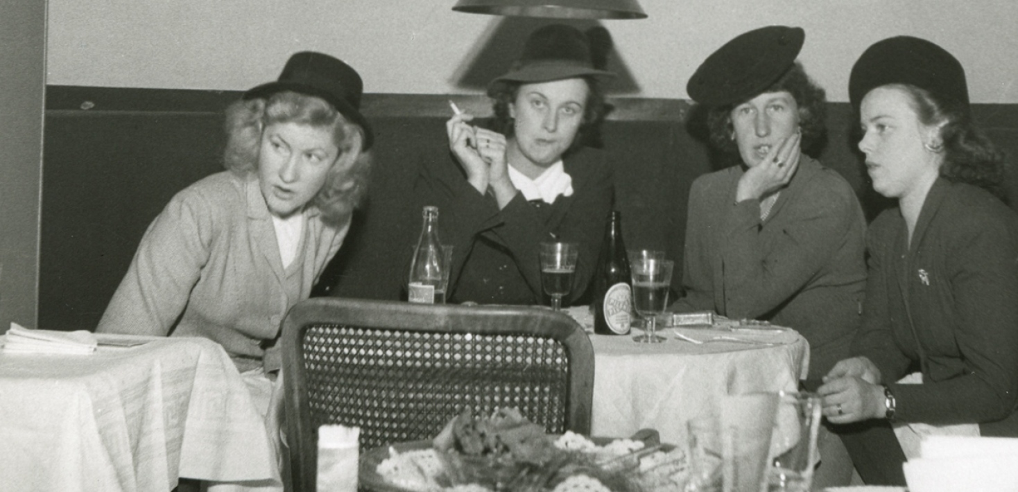 svartvitt foto. Fyra kvinnor sitter vid ett resaturangbord. En har en cigarett i handen. 