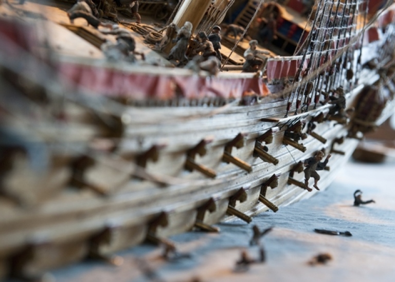 Närbild av ett skeppsmodell av örlogsfartyg. Kanonluckor öppna och skeppet lutar lite.