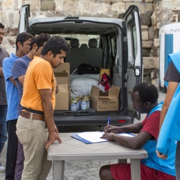 Refugees standning in front of a table belonging to UNHCR.