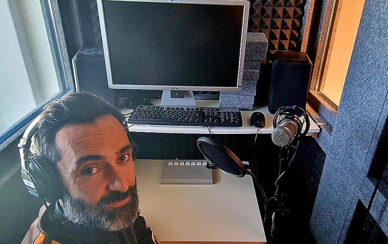 José with headphones looking up at the camera. Computer screen and mike in the background.