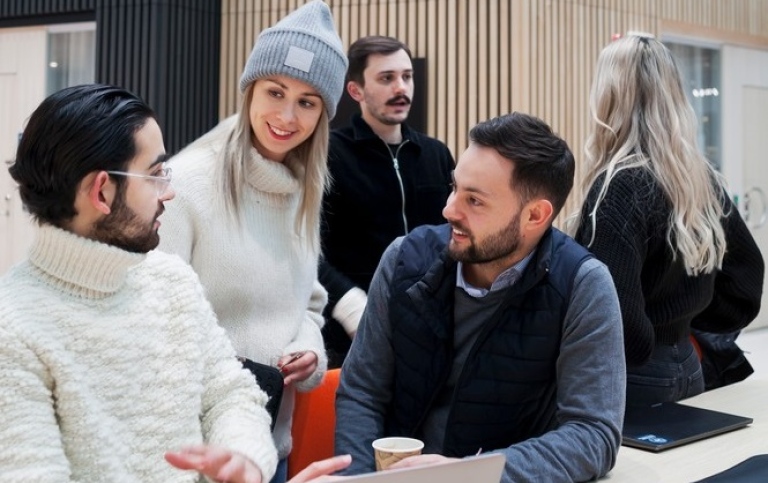 A group of students chatting in front of a laptop.