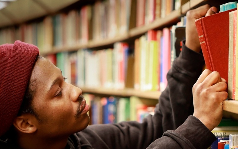 Student picking a book from a shelf in a library