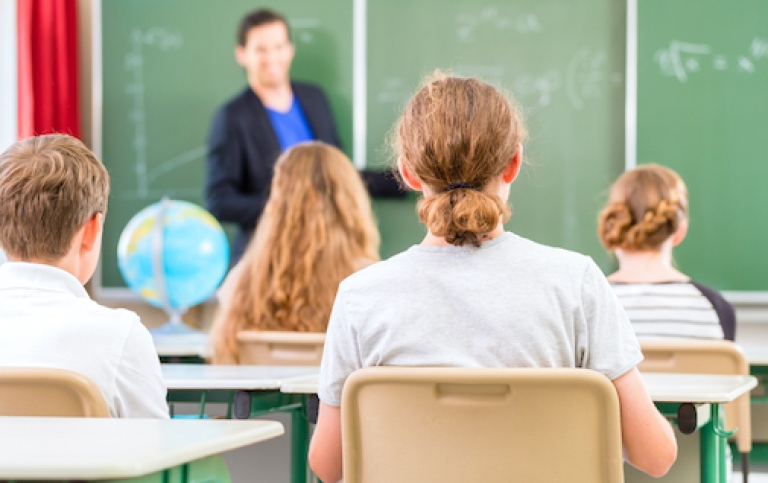 Elever har mattelektion i ett klassrum, en flicka sitter med ryggen mot kameran, en lärare ler