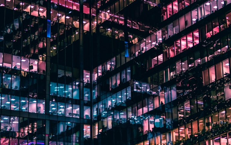 Genre photo: Office building with many floors, rooms lit in different colors. Illustrates research. 