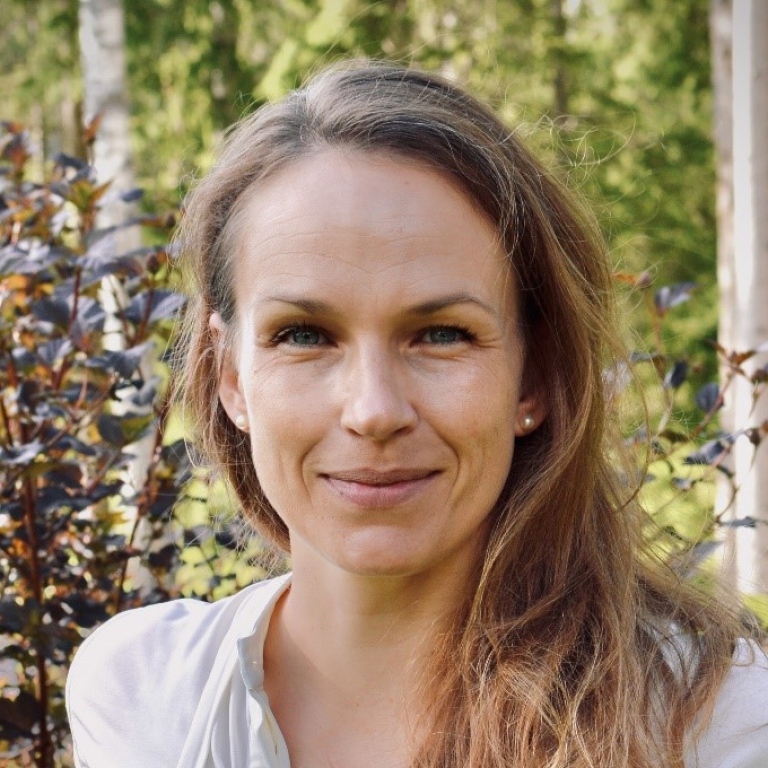 Portrait photo of a smiling woman infront of trees and bushes