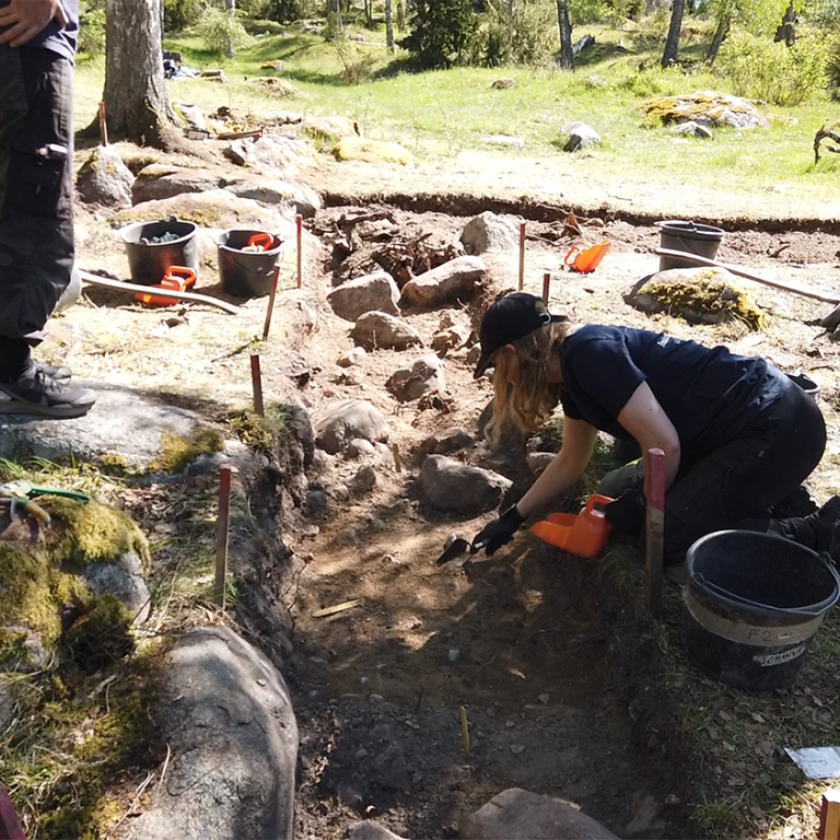 Utgrävningar på Birka våren 2022. vinklad grop i marken med arkeolger som gräver.