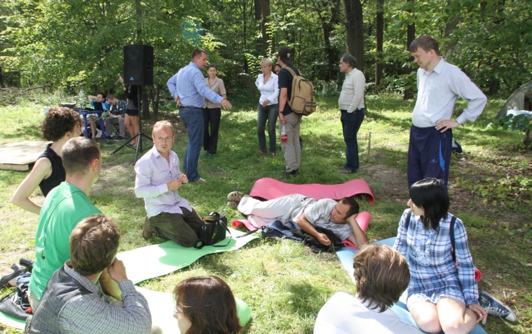 Grupp av människor sittande i skog, ser ut som att de lär sig något tillsammans.