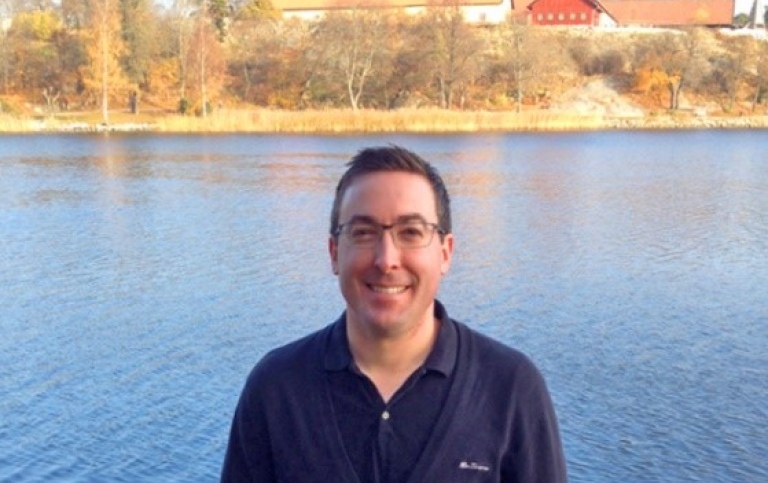 Portait of smiling man in blue sweater in front of a lake