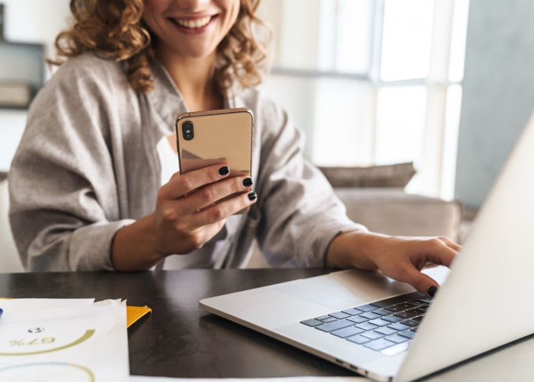 Happy female student sitting looking at her smartphone and laptop. Photo: Mostphotos/Dean Drobot.