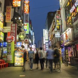 A big Korean city in the evening, with glowing signs and people on a pedestrian street