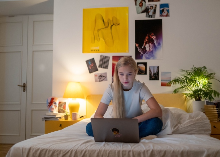 Tonåring sitter på sitt rum med dator i knät