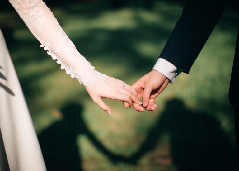 Bröllopspar håller varandra i händerna.