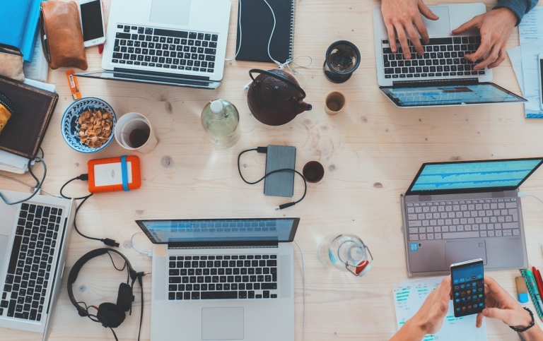 Arbetsbord med datorer, kaffekoppar mm från ovan. Foto: Marvin Meyer från Unsplash