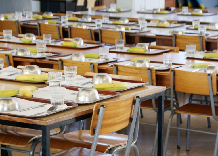 A school canteen with small tables, plates, bananas and glasses