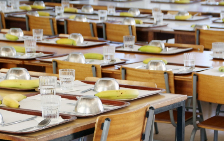  A school canteen with small tables, plates, bananas and glasses 