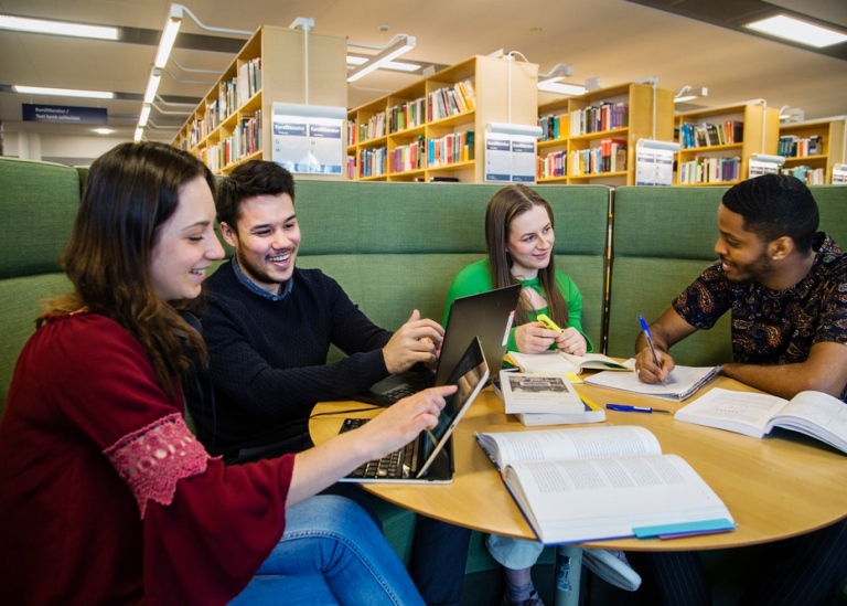 En grupp studenter diskuterar vid bord på universitetsbibliotek. Foto: Lena Katarina Johansson.
