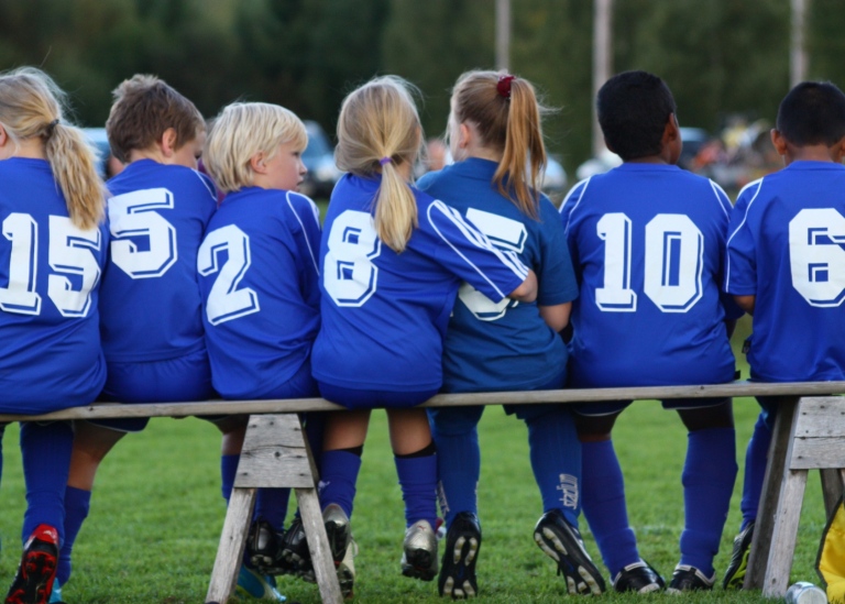 Children with football shirts are sitting on a bench