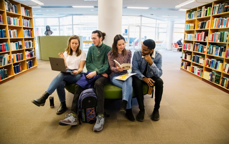 Studenter sitter tillsammans på en soffa i universitetsbiblioteket