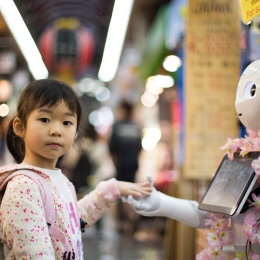 Genrebild: Ett barn och en robot håller varandra i händerna. Foto: Andy Kelly/Unsplash.