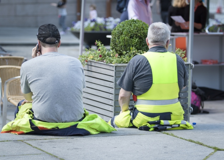 Två byggarbetare sitter med ryggen mot kameran och har paus i sitt arbete