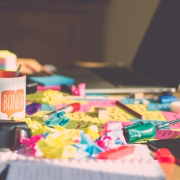 Oordnat skrivbord med dator, kaffekopp och post-it-lappar. Foto: Ferenc Horvath på Unsplash.