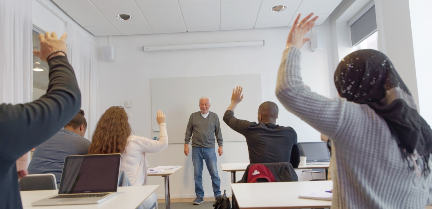 Vuxna elever i ett klassrum räcker upp handen.