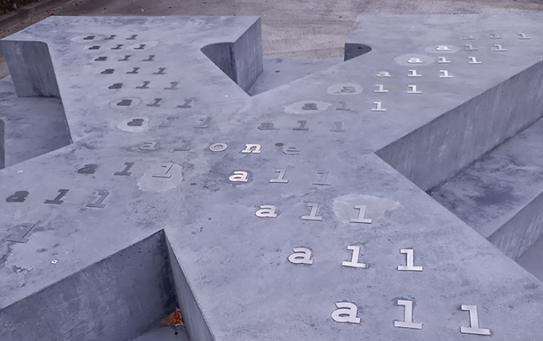 Monument i betong i form av bokstaven X liggande med text på 