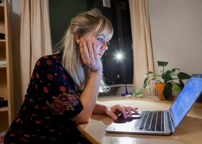 Ung kvinna sitter och läser på Laptop vid skrivbord på kvällen.