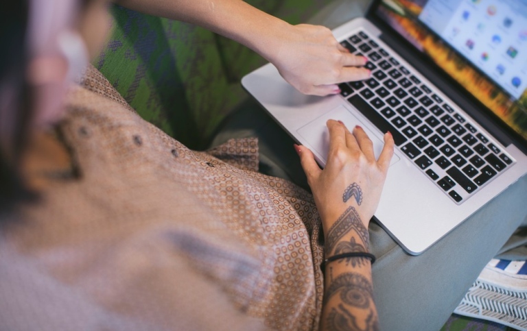 Woman sitting and writing on laptop in her knee. 