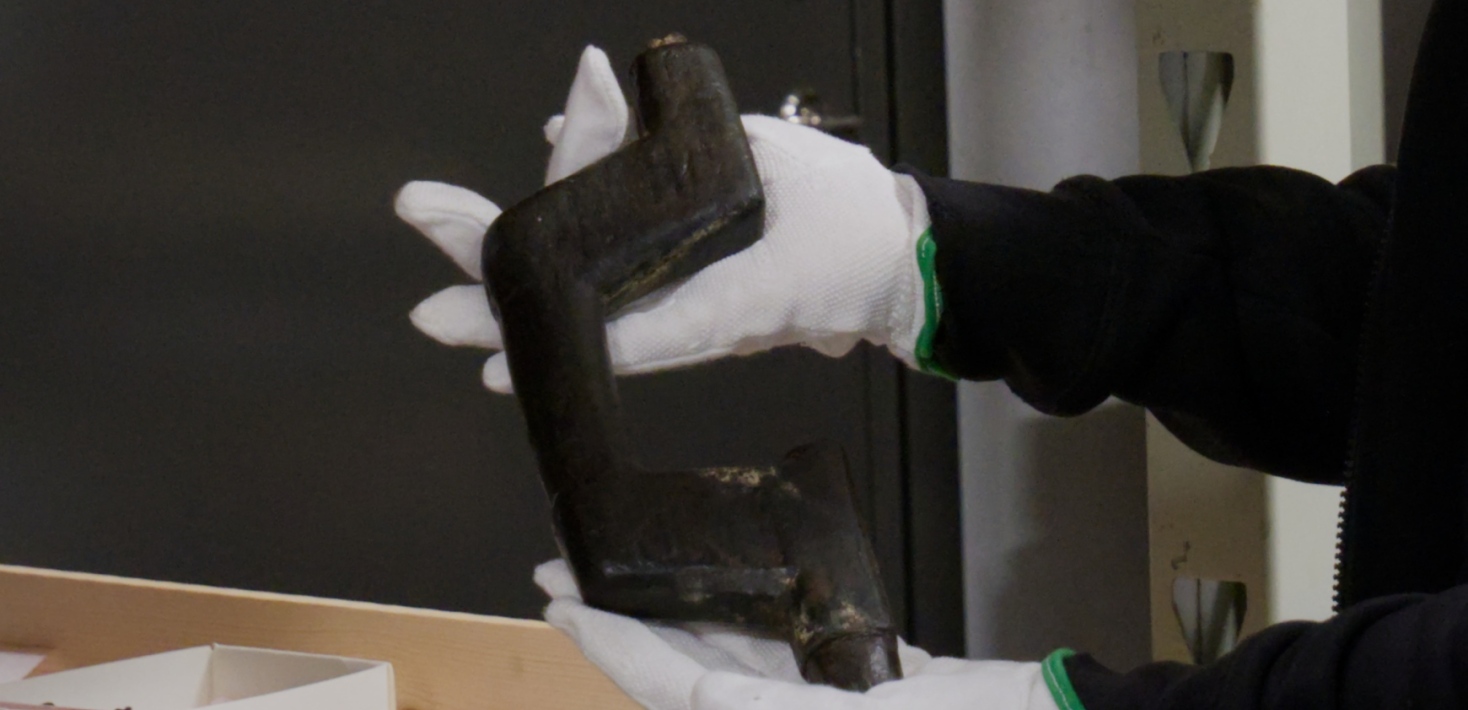 Händer med vita handskar håller i mörkt träföremål